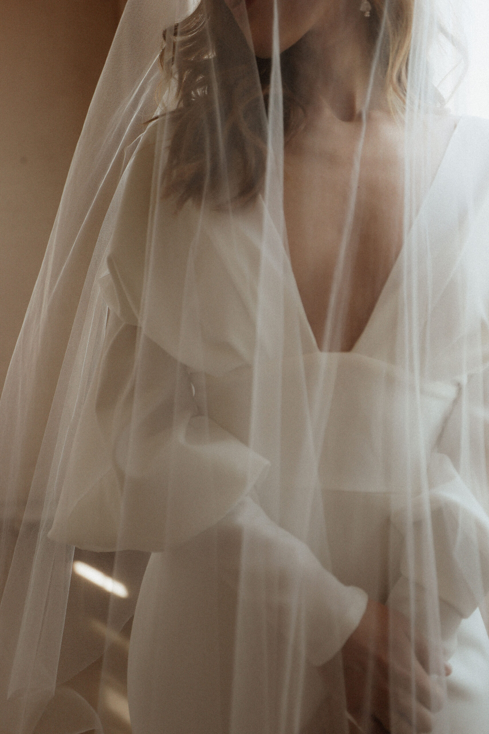 A close-up of a bride in a modern, elegant gown with a delicate veil softly draped over her, creating a timeless and intimate moment.