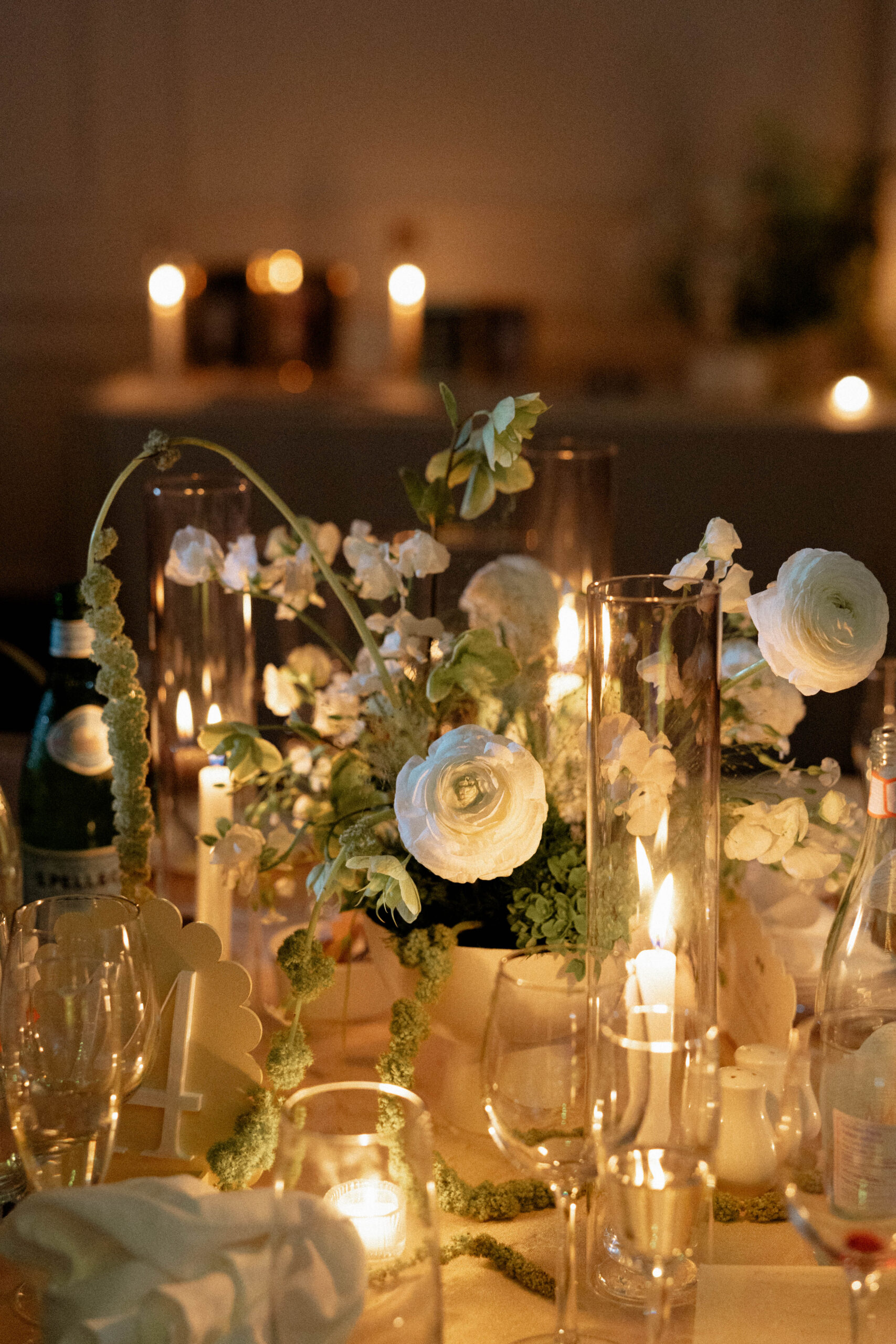 "A romantic, candlelit wedding reception table adorned with elegant white floral arrangements, delicate greenery, and glowing candles, creating a warm and intimate ambiance.