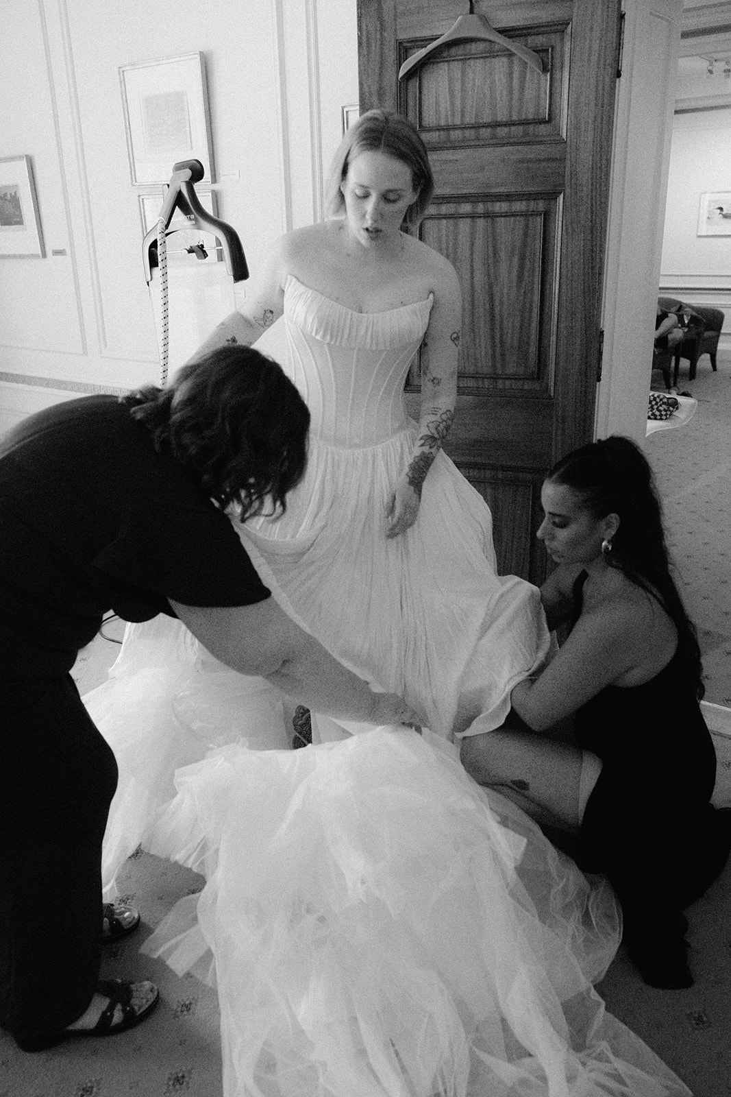 Bride in a strapless corset gown with tulle skirt being helped into her dress by two attendants while getting ready at the University Club of Toronto