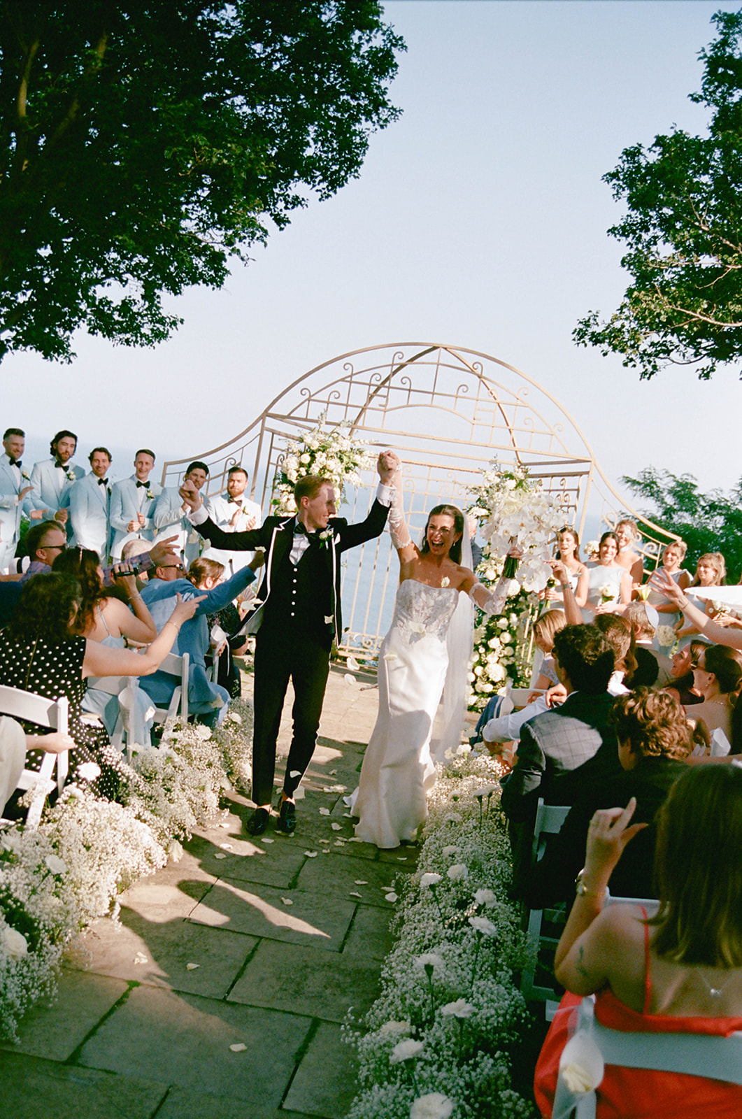 Shannon and Cameron raising their hands in celebration as they walk back up the aisle at their Toronto Hunt wedding, guests cheering on either side.